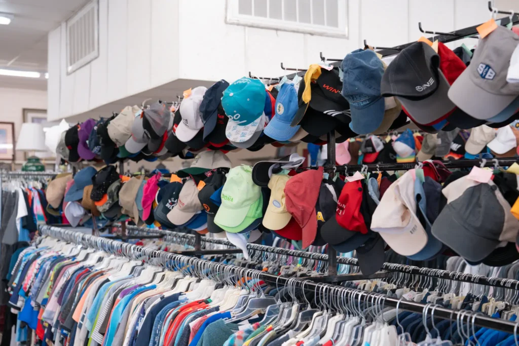 Large selection of secondhand baseball caps displayed above clothing racks at the Value World Gessner location.