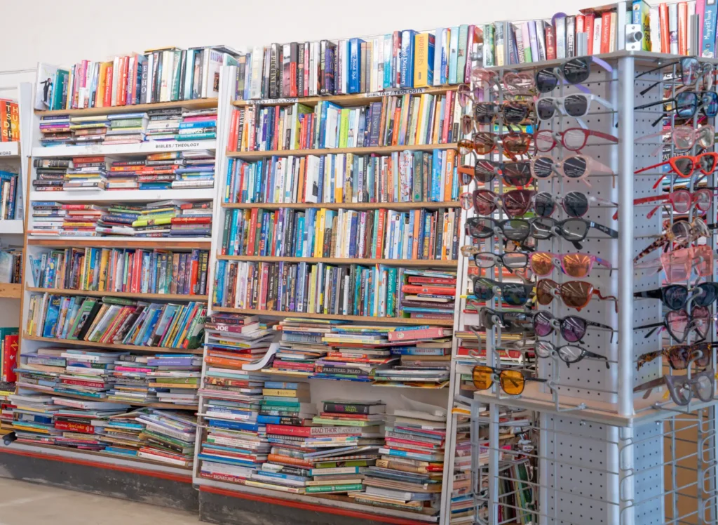 Shelves filled with secondhand books beside a display of sunglasses and eyeglasses at the Gessner thrift store.
