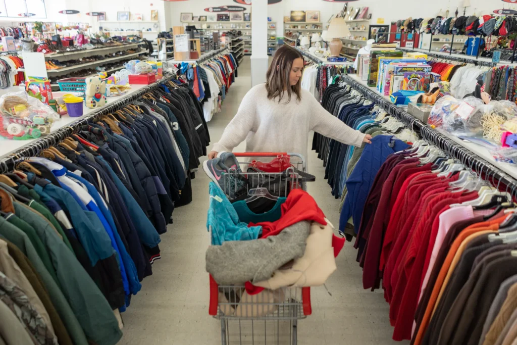 Shopper browsing colorful sweaters and jackets with a full shopping cart inside the Value World Lakewood location.