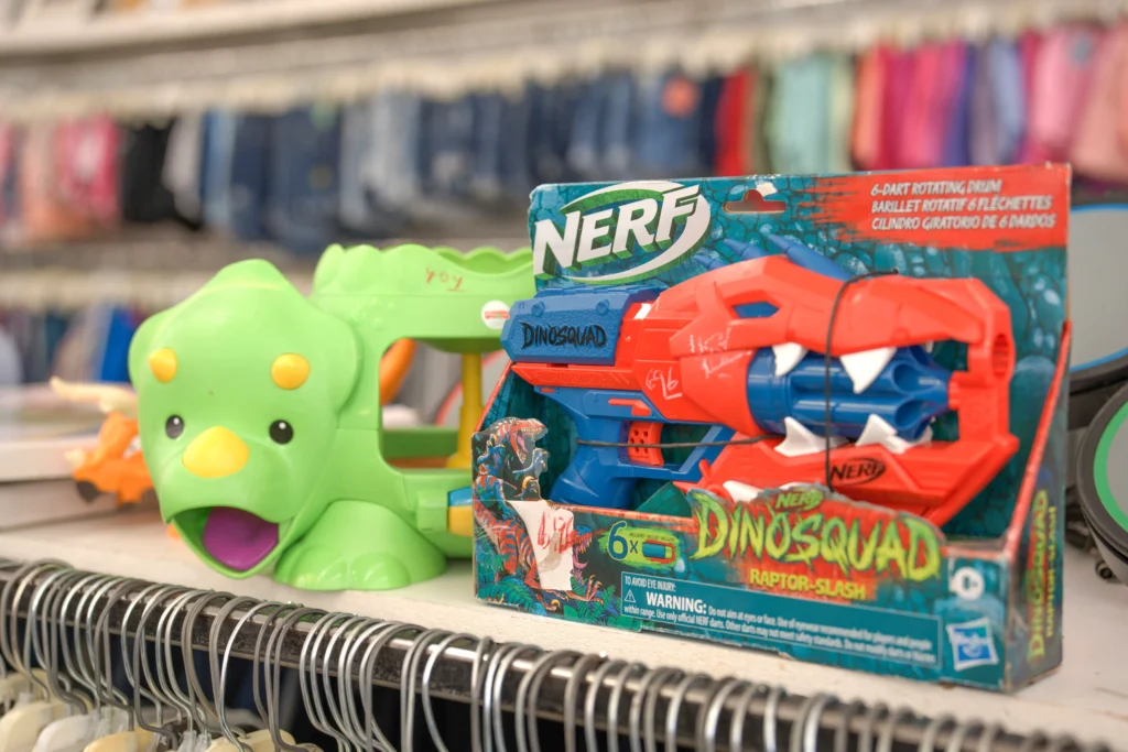 Dinosaur-themed toys and a Nerf blaster displayed above clothing racks at the Value World The Heights