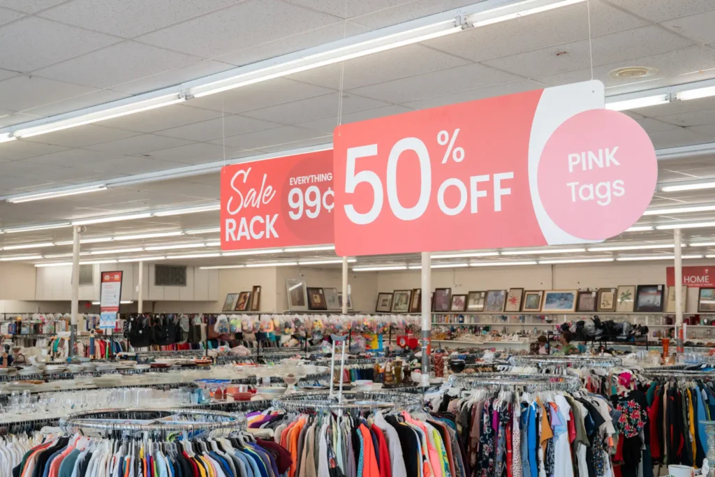 Clothing racks and housewares beneath pink-tag discount signs inside the Value World Gessner location.