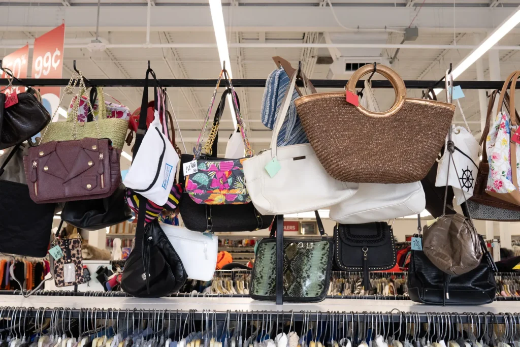 A variety of handbags and purses displayed above clothing racks inside a Value World store.