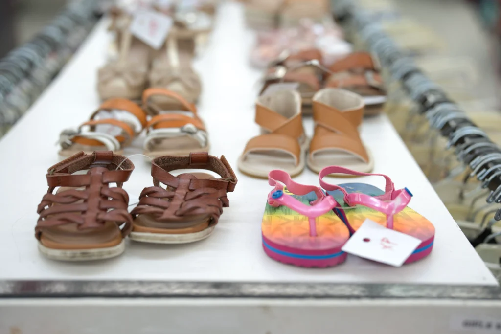 Colorful children’s sandals and summer shoes displayed above clothing racks at The Heights location.