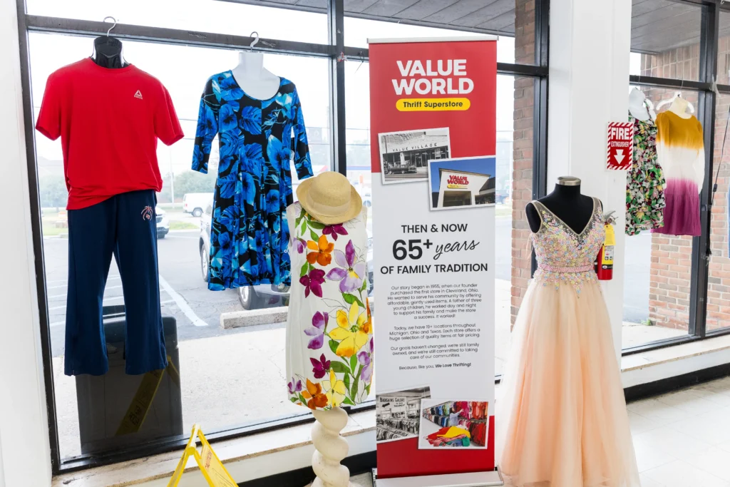 Mannequins dressed in casual clothing, floral dresses, and a formal gown beside a Value World history display.