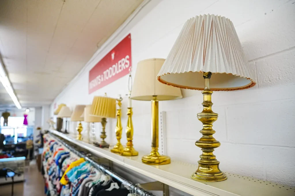 A row of brass and neutral-colored table lamps displayed above clothing racks inside Value World.