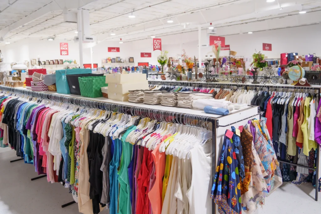 Wide interior view of colorful clothing racks, storage baskets, home decor, and sale signs inside Value World Barker Cypress.